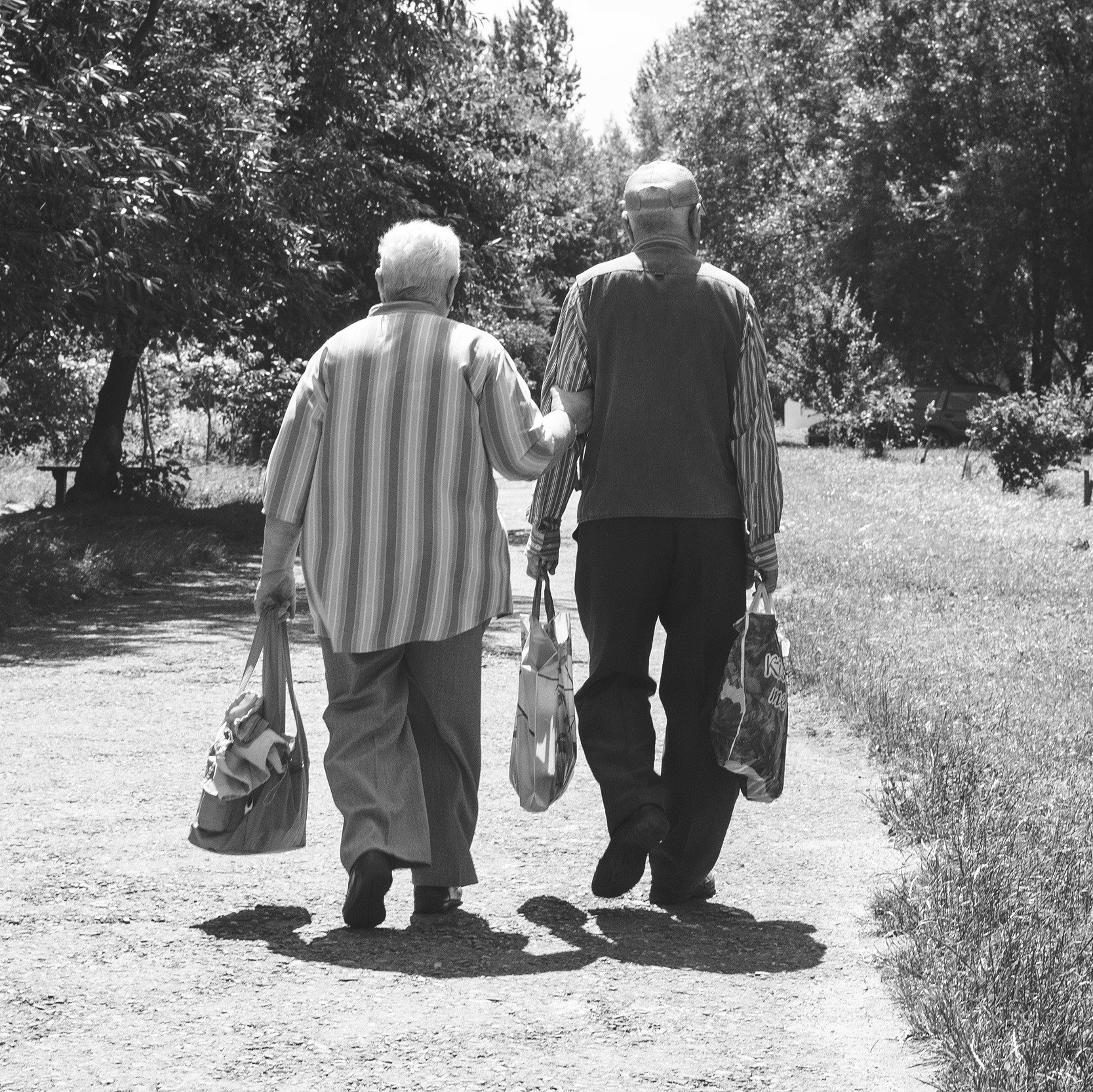An elderly pair walking and lifting bags