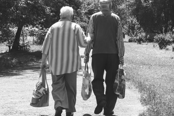 An elderly pair walking and lifting bags